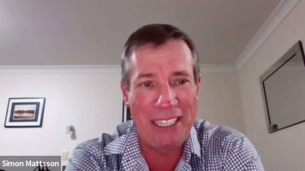 A man with short hair is speaking during a video call. He is wearing a checkered shirt and is indoors, with framed pictures and a mirror on the wall behind him. The name "Simon Mattsson" is displayed at the bottom left corner of the image.